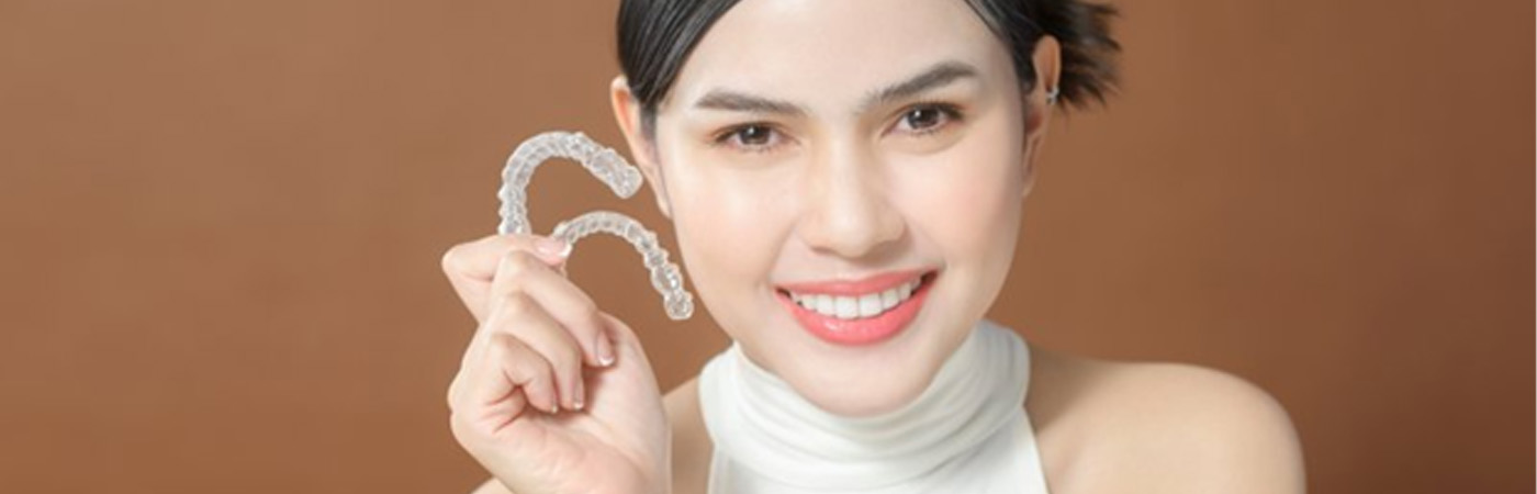 Lady smiles while holding clear aligners