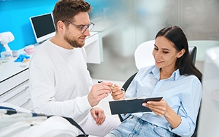Man handing clipboard with forms and pen to patient in dental chair