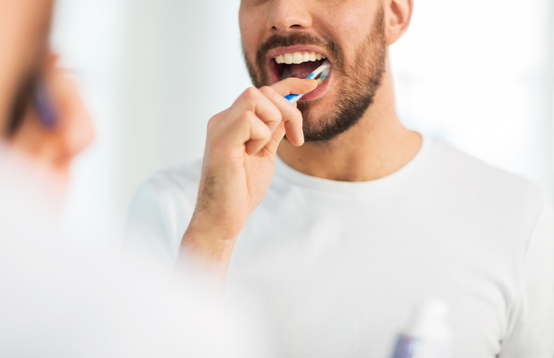 Patient with dental implants brushing their teeth in mirror